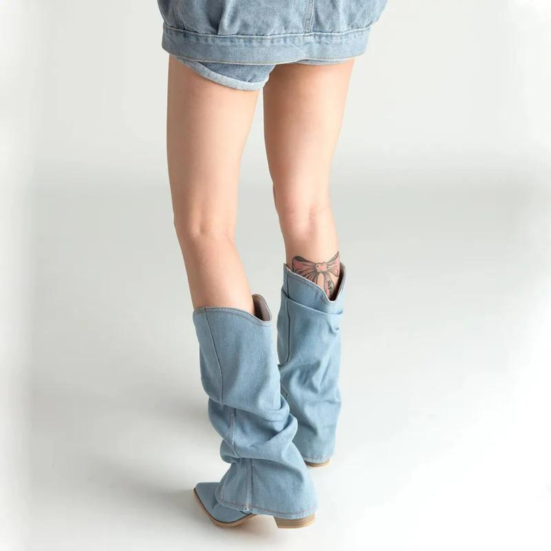 Frau in blauen Jeans-Shorts und hellblauen Cowboy-Stiefeln mit Tattoo am Bein. Modetrend, Denim-Look, Sommeroutfit, Streetstyle.