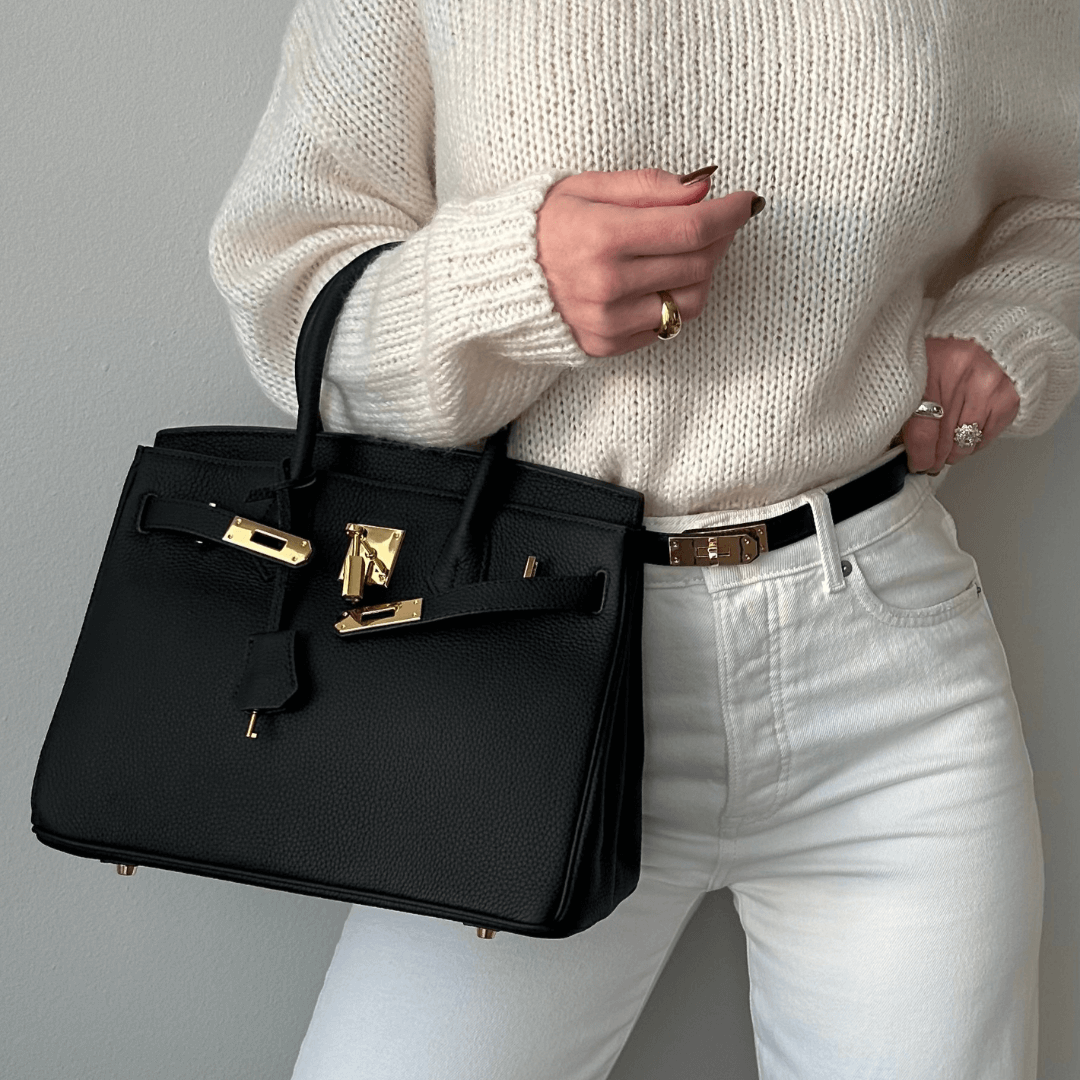 Frau mit schwarzer Designer-Handtasche, weißem Strickpullover und weißer Jeans. Elegante Mode, Luxusaccessoire, stilvolles Outfit.