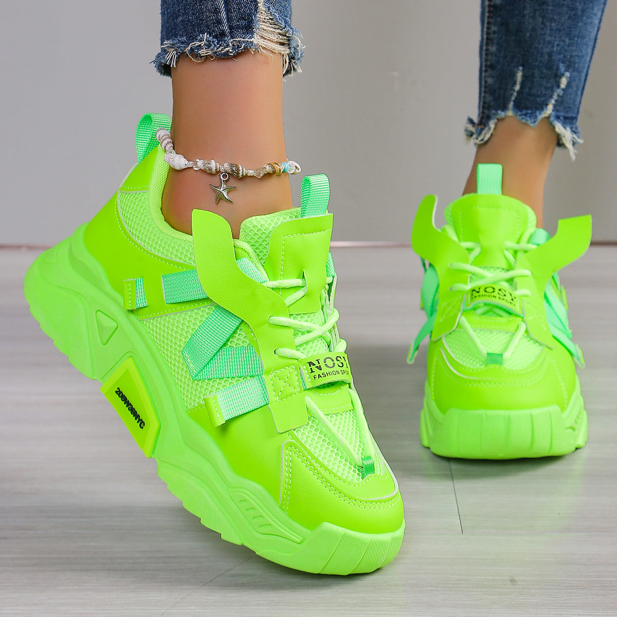 Neon-grüne Sneaker mit dicker Sohle, getragen von Person mit Jeans und Fußkettchen. Modische Sportschuhe, auffälliges Design, trendige Damenmode.
