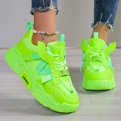Neon-grüne Sneaker mit dicker Sohle, getragen von Person mit Jeans und Fußkettchen. Modische Sportschuhe, auffälliges Design, trendige Damenmode.