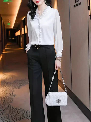 Elegante Frau in weißer Bluse und schwarzer Hose, hält weiße Handtasche. Stilvolle Mode im modernen Hotelflur. Business-Look, Damenmode.