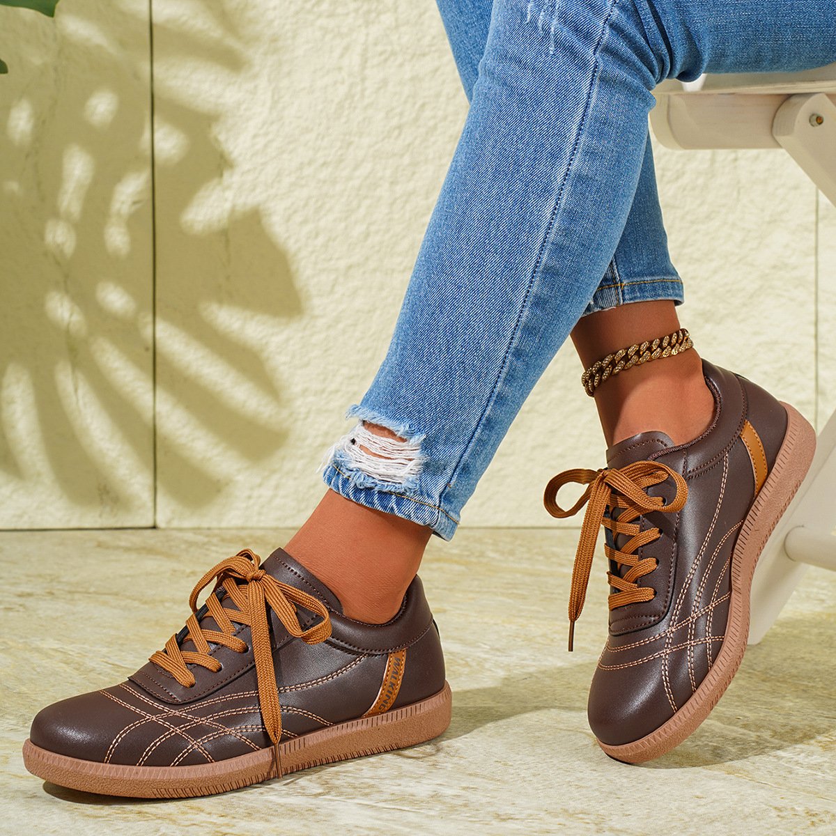Braune Damen-Sneaker mit hellbraunen Schnürsenkeln, getragen zu blauen, zerrissenen Jeans. Modische Freizeitschuhe, ideal für den Alltag.