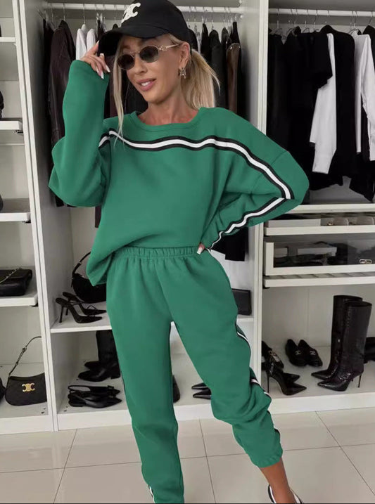 Frau in grünem Trainingsanzug und schwarzer Kappe posiert vor Kleiderschrank. Modetrend, sportlich-elegant, Damenbekleidung, Freizeitlook.