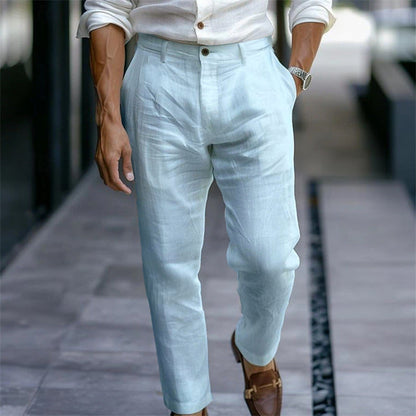 Mann in hellblauer Leinenhose und weißem Hemd, braune Loafer, eleganter Sommerlook, modisch, urbaner Stil, Gehweg im Hintergrund.