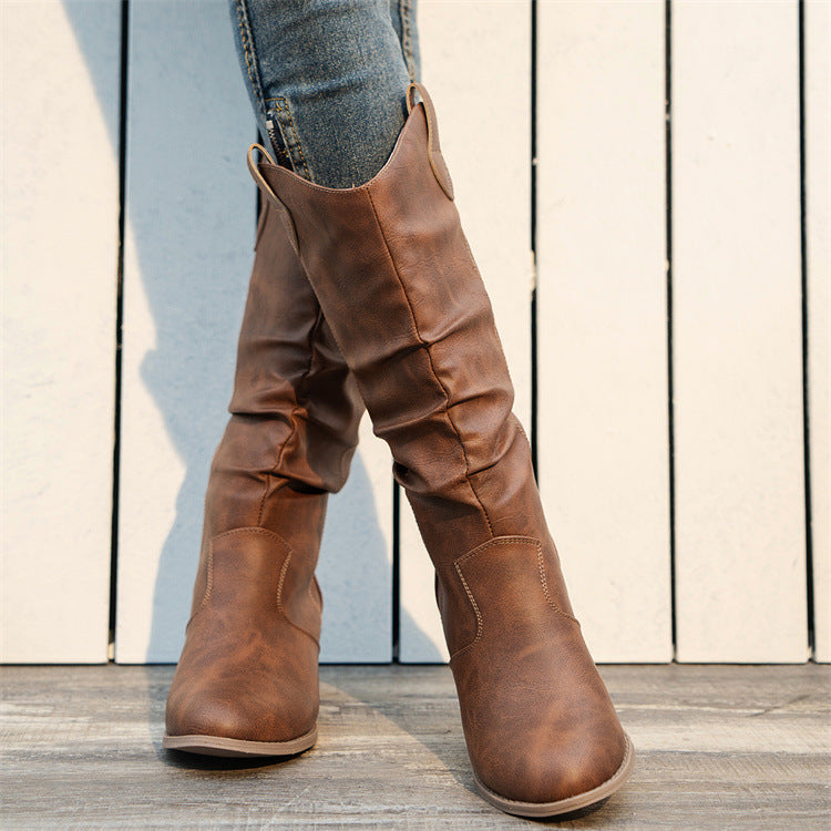 Braune Cowboystiefel aus Leder auf Holzboden, getragen mit blauen Jeans. Modische Damenstiefel, ideal für Herbstmode und Western-Look.