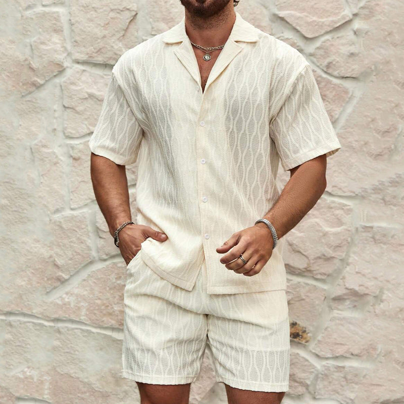 Mann in weißem Leinenhemd und Shorts vor Steinwand. Sommermode, Herrenbekleidung, lässiger Stil, elegantes Design, Freizeitoutfit.
