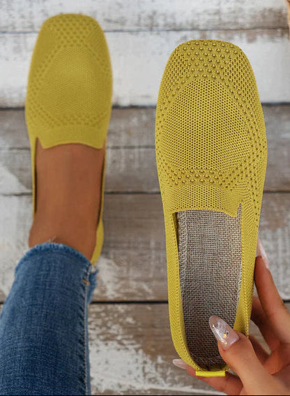 Gelbe Damen-Loafer aus Strickmaterial, getragen von einer Person in blauen Jeans auf Holzboden. Bequeme, atmungsaktive Freizeitschuhe.