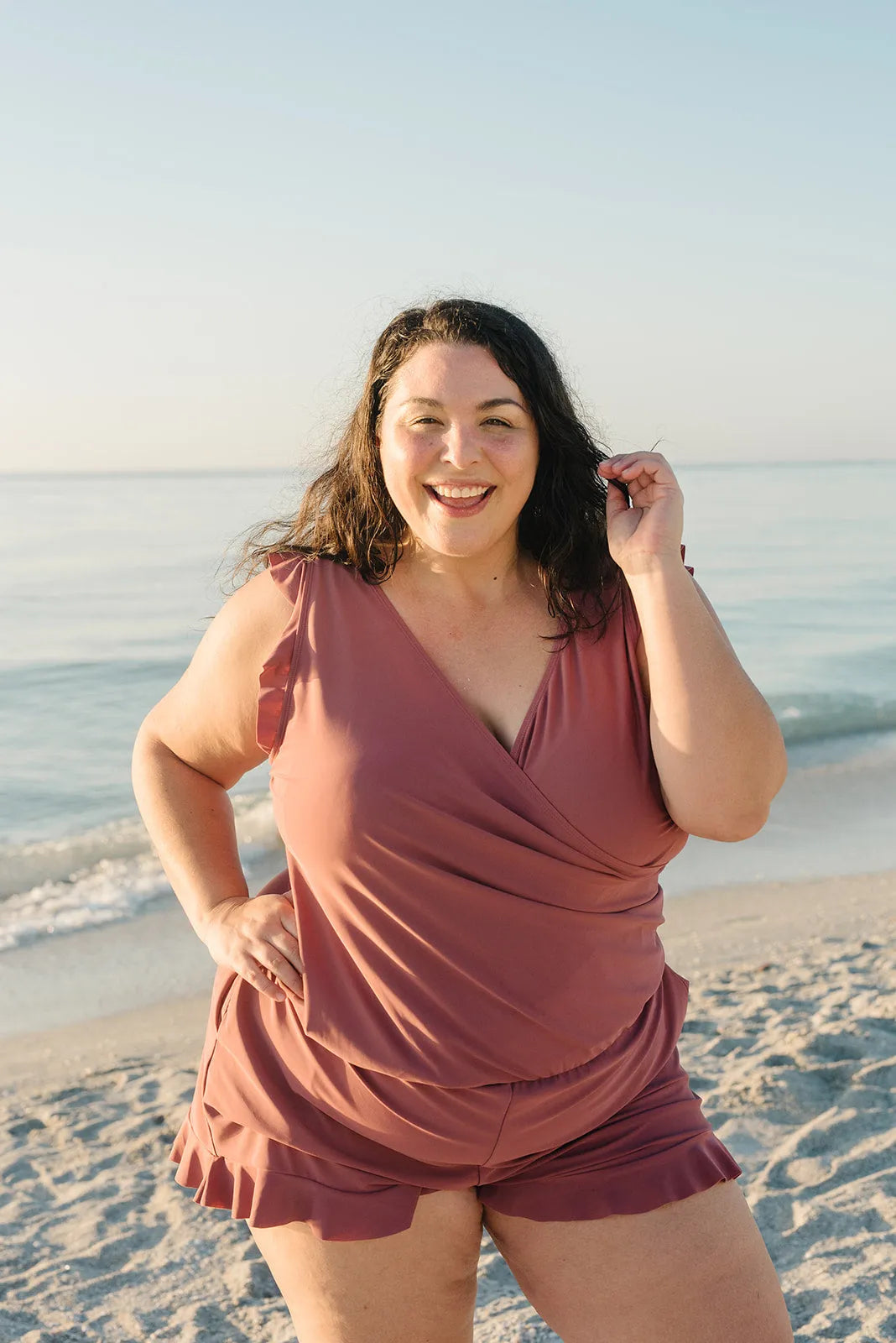 Frau in rosa Strandkleidung lächelt am Meer, sonniger Tag, entspannter Strandspaziergang, Sommermode, Urlaub am Meer, Freizeitkleidung.