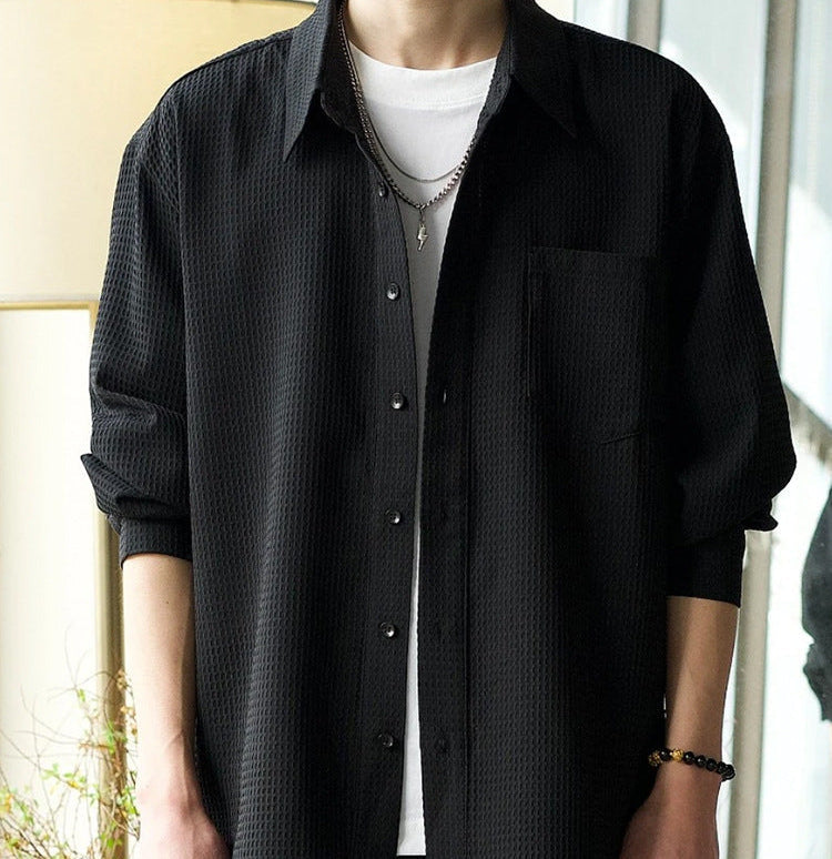 Schwarzes Herrenhemd mit Knopfleiste, lässig über weißem T-Shirt getragen. Modischer Look, ideal für Freizeit und Streetwear.