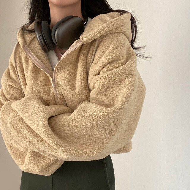 Frau in beiger Teddyfleece-Jacke mit Kapuze und schwarzen Kopfhörern um den Hals, modisch und gemütlich, Herbstmode, Streetwear-Trend.