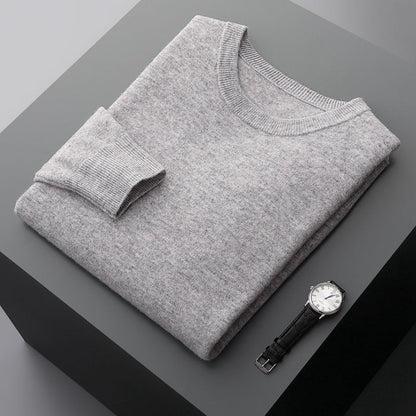 Grauer Pullover aus Kaschmir auf grauem Tisch, daneben eine elegante Armbanduhr mit schwarzem Lederarmband. Mode, Luxus, Herrenbekleidung.