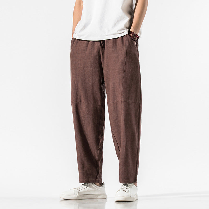 Person trägt braune Leinenhose, kombiniert mit weißem T-Shirt und weißen Sneakers. Modetrend, lässiger Stil, Herrenbekleidung, komfortable Passform.
