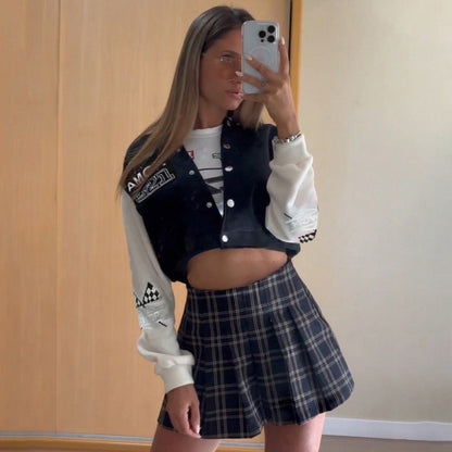 Junge Frau im karierten Rock und Collegejacke macht Selfie im Spiegel. Modetrend, Streetstyle, lässiges Outfit, modische Kleidung.