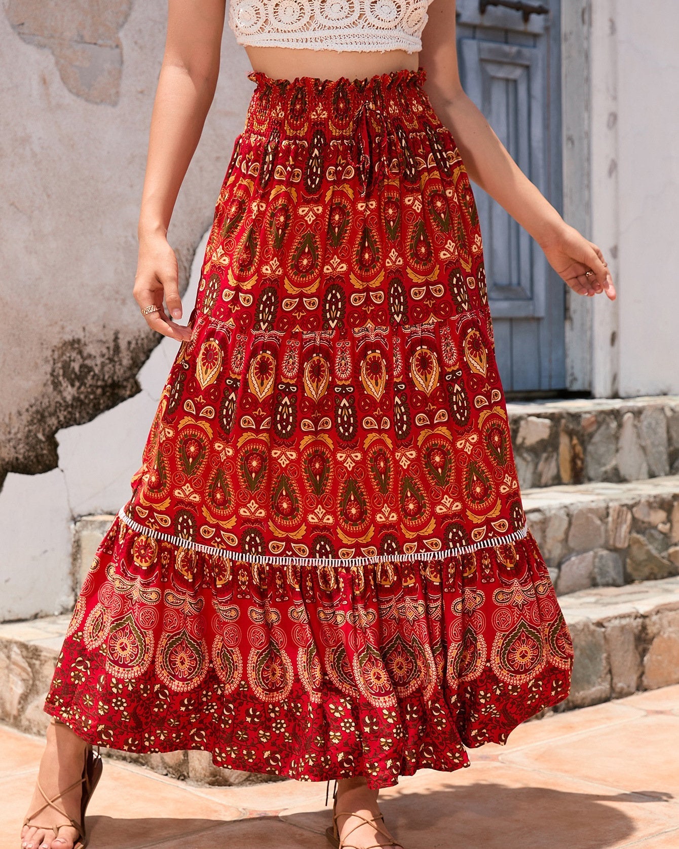 Frau in rotem, gemustertem Maxirock vor rustikalem Hintergrund. Boho-Chic, Sommermode, Damenbekleidung, modischer Maxirock, Ethno-Design.