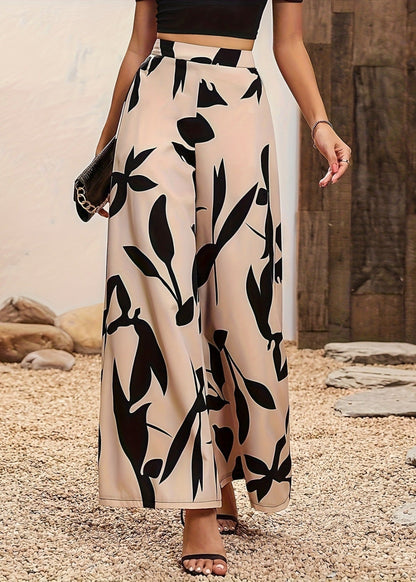 Frau in eleganter, hoch taillierter, schwarz-weiß gemusterter Palazzohose, kombiniert mit schwarzem Oberteil und Sandalen, auf Kiesweg.