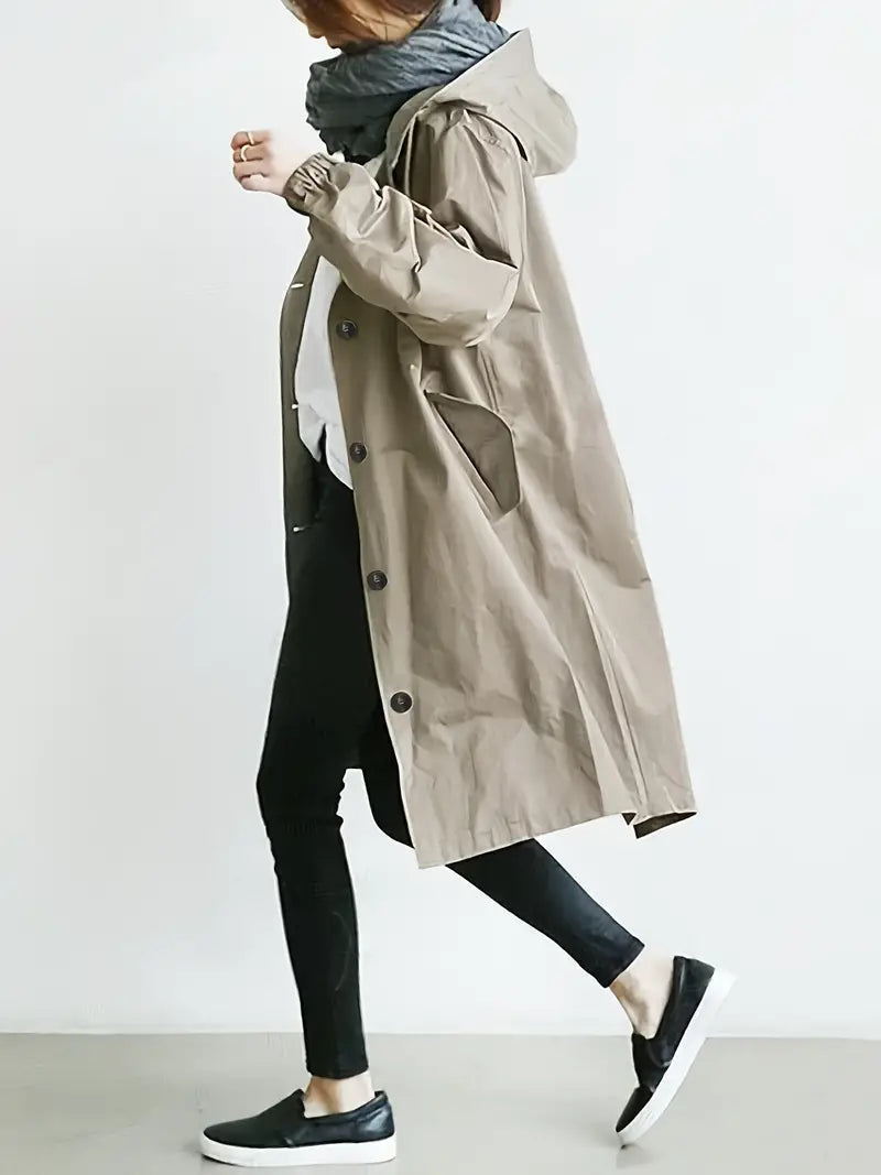 Frau in beigem Trenchcoat, schwarzer Hose und Sneakers, seitlich gehend. Modischer Herbstlook, lässiger Stil, Streetwear, Damenmode.