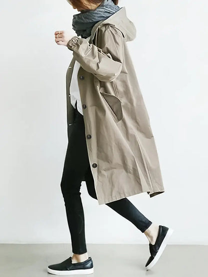 Frau in beigem Trenchcoat, schwarzer Hose und Sneakers, seitlich gehend. Modischer Herbstlook, lässiger Stil, Streetwear, Damenmode.