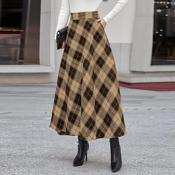 Dame in weißem Pullover und kariertem Maxirock, kombiniert mit schwarzen Stiefeletten, steht auf grauem Pflaster. Elegante Herbstmode, stilvoller Look.