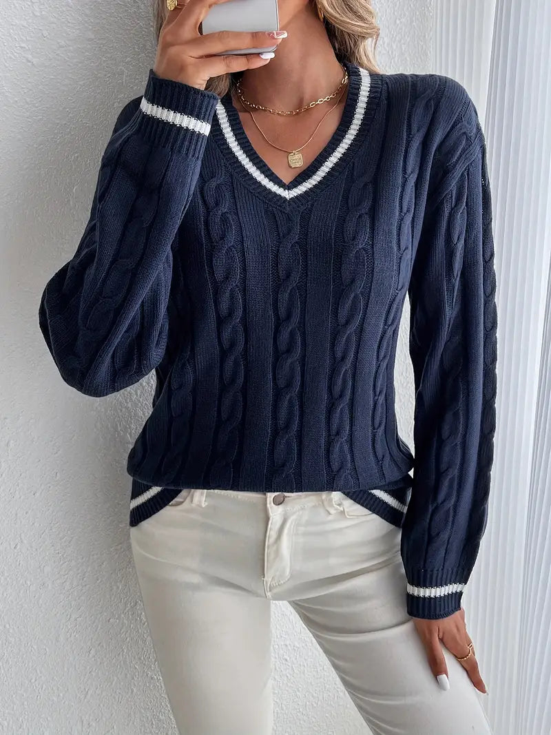 Frau in dunkelblauem Zopfmuster-Pullover mit V-Ausschnitt und weißen Streifen, kombiniert mit weißen Jeans. Elegante Herbstmode, lässiger Stil.