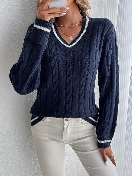 Frau in dunkelblauem Zopfmuster-Pullover mit V-Ausschnitt und weißen Streifen, kombiniert mit weißen Jeans. Elegante Herbstmode, lässiger Stil.