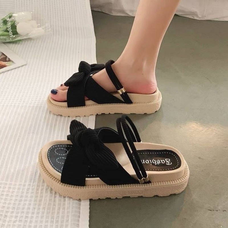 Schwarze Damen-Sandalen mit Schleife, flache Sohle und elastischen Riemen, ideal für Sommermode und Freizeitkleidung.
