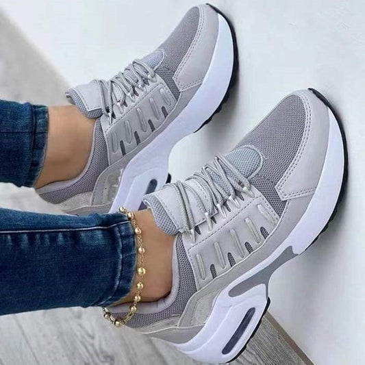 Graue Damen-Sneaker mit weißer Sohle, getragen mit blauer Jeans und goldener Fußkette. Modische Sportschuhe, bequem und stilvoll.