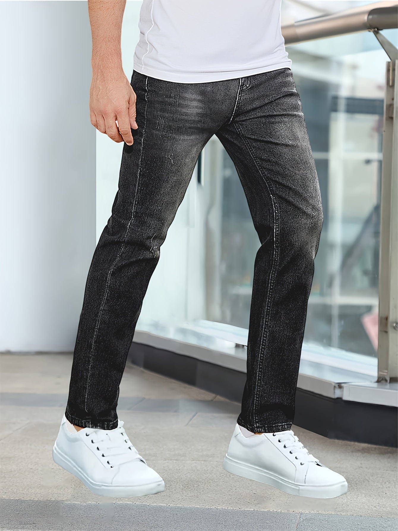 Mann in schwarzer Jeans und weißen Sneakers, stehend auf modernem Gehweg. Modische Herrenbekleidung, lässiger Stil, urbane Mode.