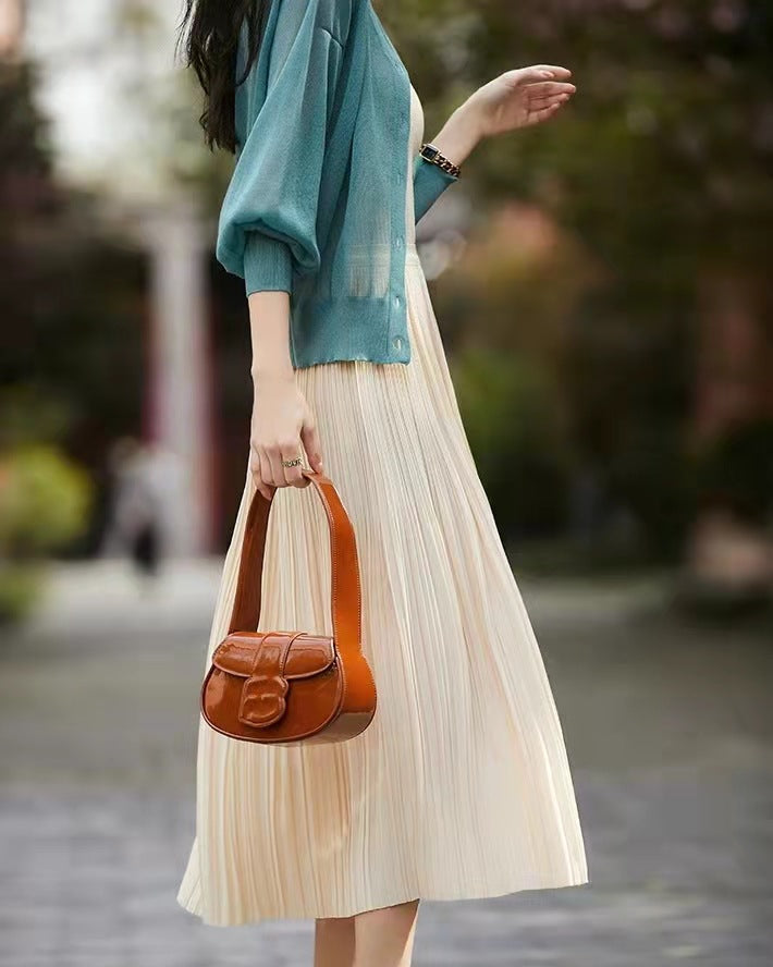 Frau in blauem Cardigan und cremefarbenem Plisseekleid, hält braune Ledertasche. Modetrend, eleganter Stil, Frühlingsoutfit.