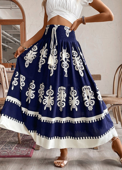 Frau in weißem Crop-Top und blau-weißem Boho-Rock mit Blumenmuster, steht in modernem Café. Sommermode, Boho-Stil, Damenbekleidung.