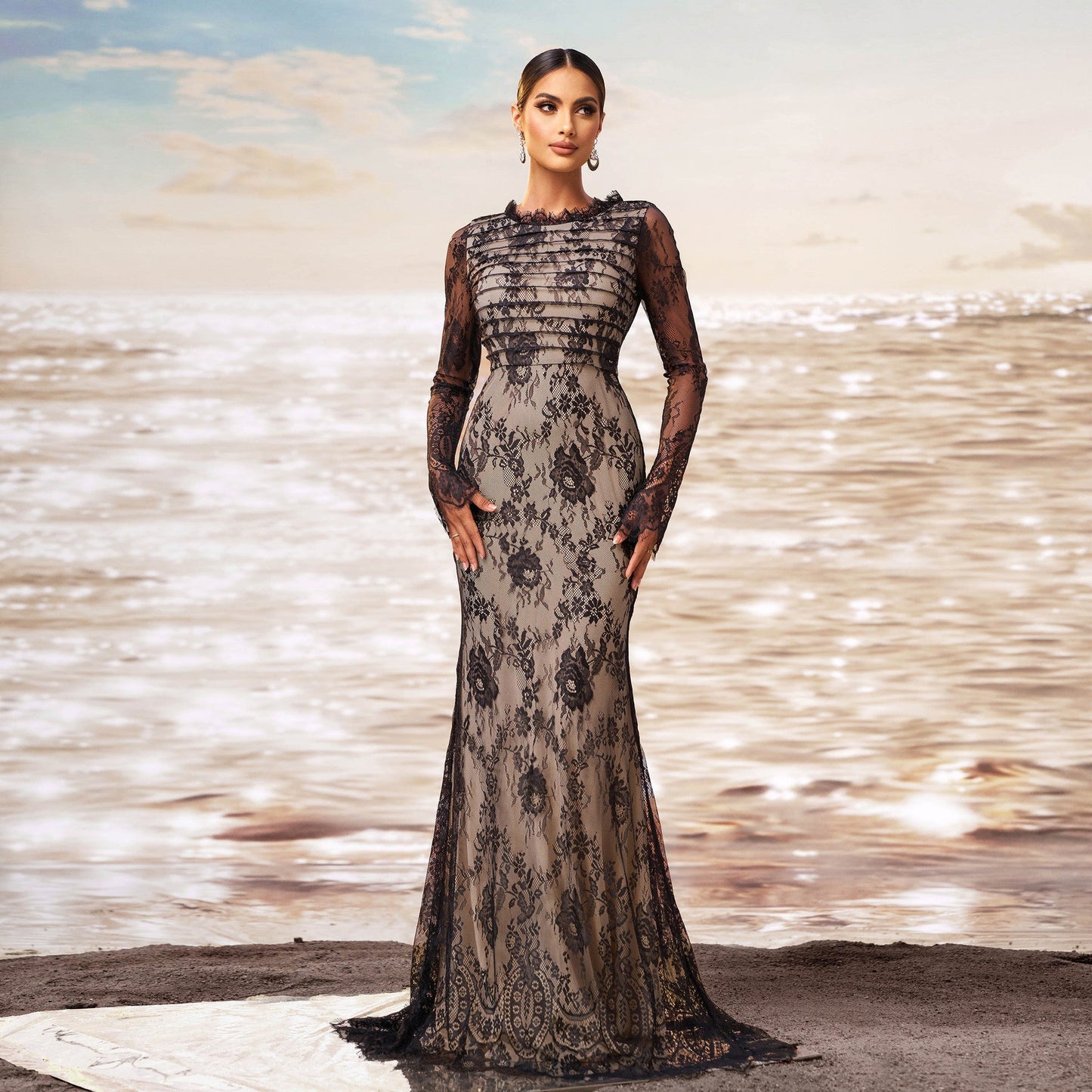 Elegante Frau in schwarzem Spitzenkleid am Strand bei Sonnenuntergang, modisches Abendkleid, stilvolle Abendmode, glamouröse Strandkulisse.