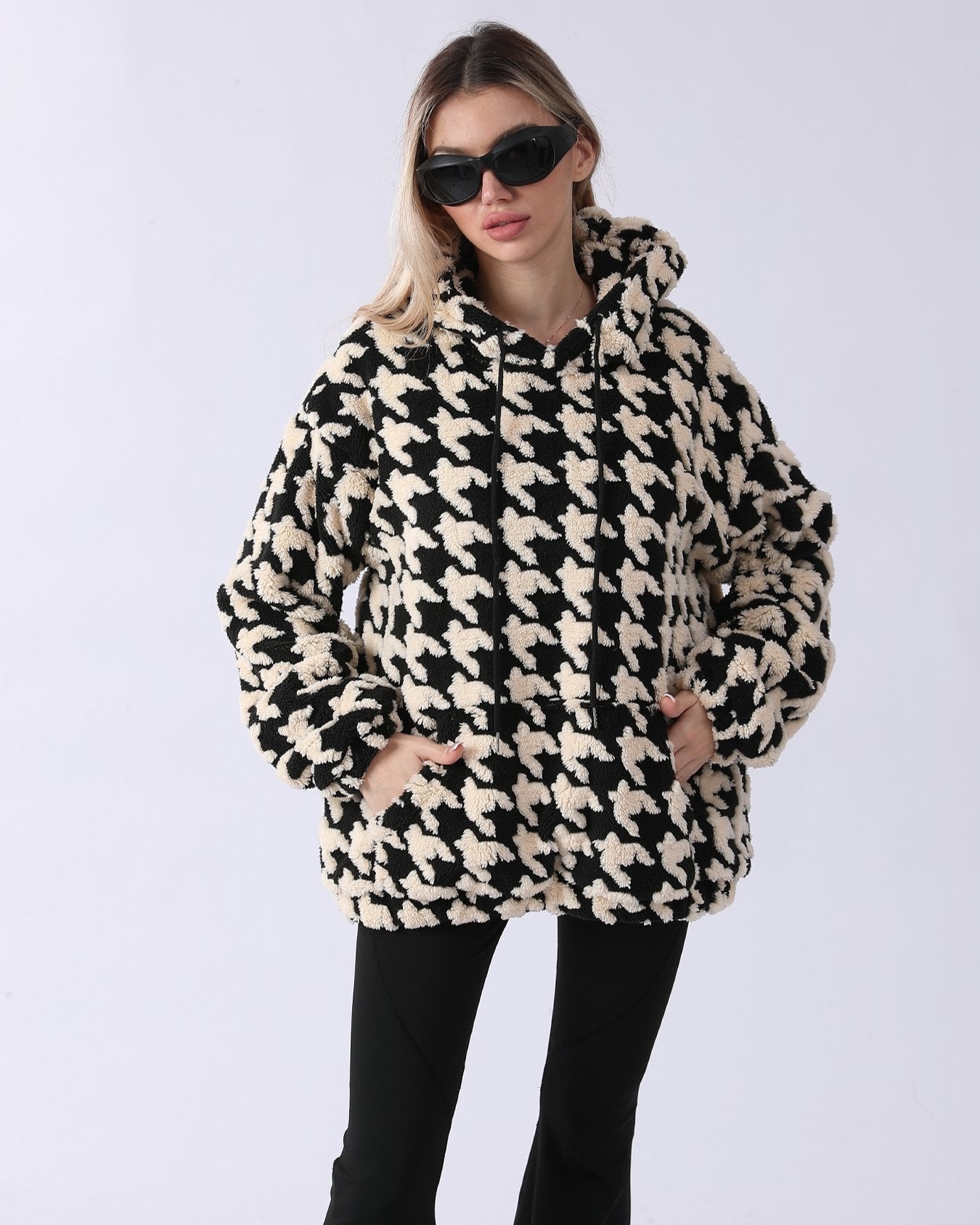 Frau in schwarz-weißem Hahnentritt-Muster Hoodie, trägt Sonnenbrille. Modetrend, Wintermode, stilvoller Look, gemütlicher Pullover.