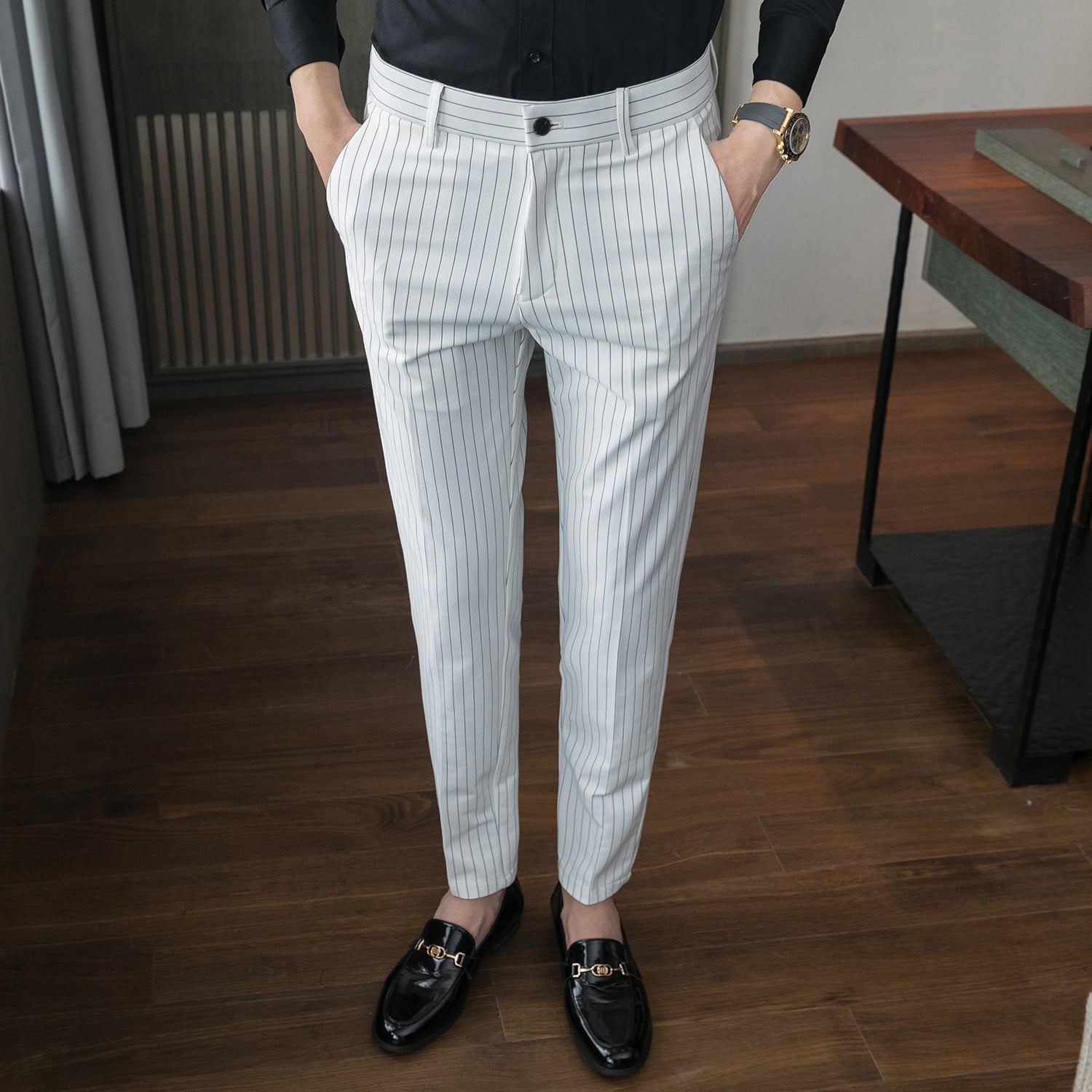 Mann in eleganter, weiß gestreifter Anzughose und schwarzen Lederschuhen, steht auf Holzboden. Businessmode, Herrenbekleidung, stilvoll.