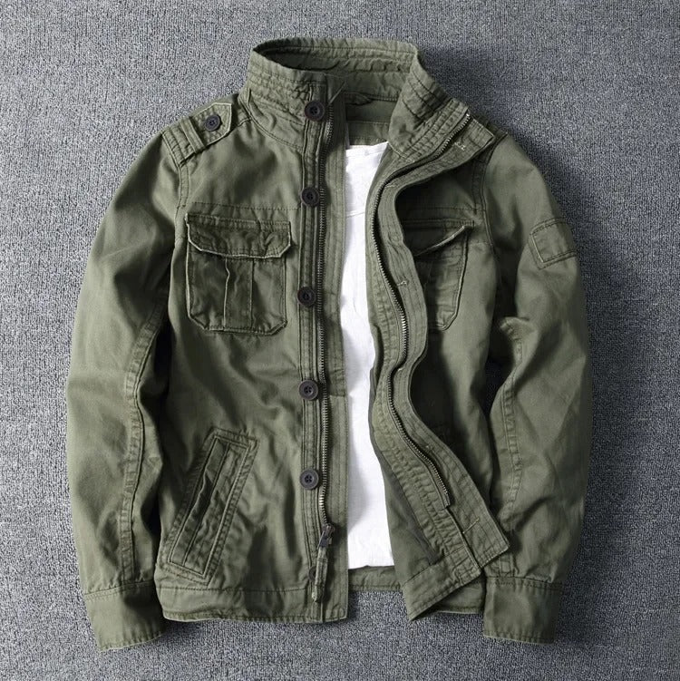 Olivgrüne Herrenjacke mit Stehkragen, Knopfleiste und mehreren Taschen auf grauem Hintergrund. Modische Outdoor-Bekleidung, lässiger Stil.