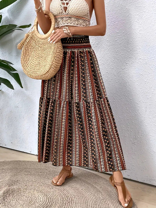 Frau in Boho-Maxirock mit Ethno-Muster, weißem Häkel-Top und Strohtasche. Sommermode, Boho-Chic, lässiger Stil.