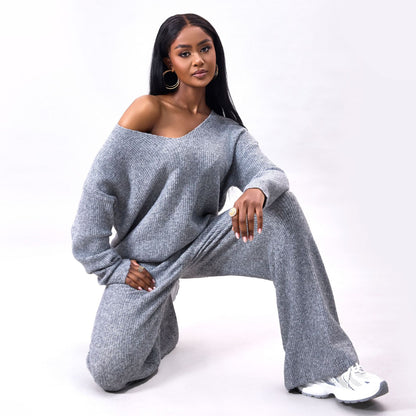 Frau in grauem Strickpullover und Hose, kniend, mit weißen Sneakers. Modetrend, gemütlicher Look, Herbstmode, stilvolle Damenbekleidung.