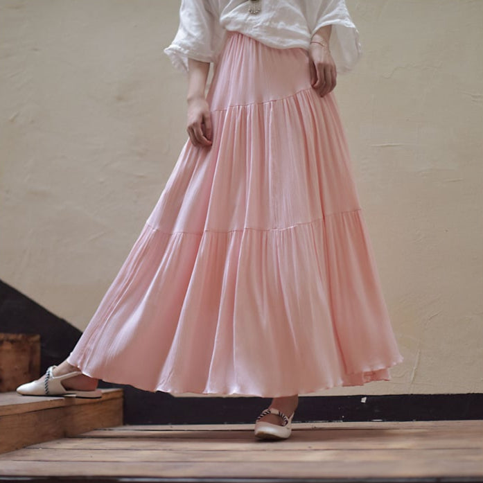 Lange rosa Maxirock aus fließendem Stoff, kombiniert mit weißer Bluse und flachen Schuhen. Elegante Damenmode, ideal für Sommeroutfits.