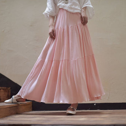 Lange rosa Maxirock aus fließendem Stoff, kombiniert mit weißer Bluse und flachen Schuhen. Elegante Damenmode, ideal für Sommeroutfits.