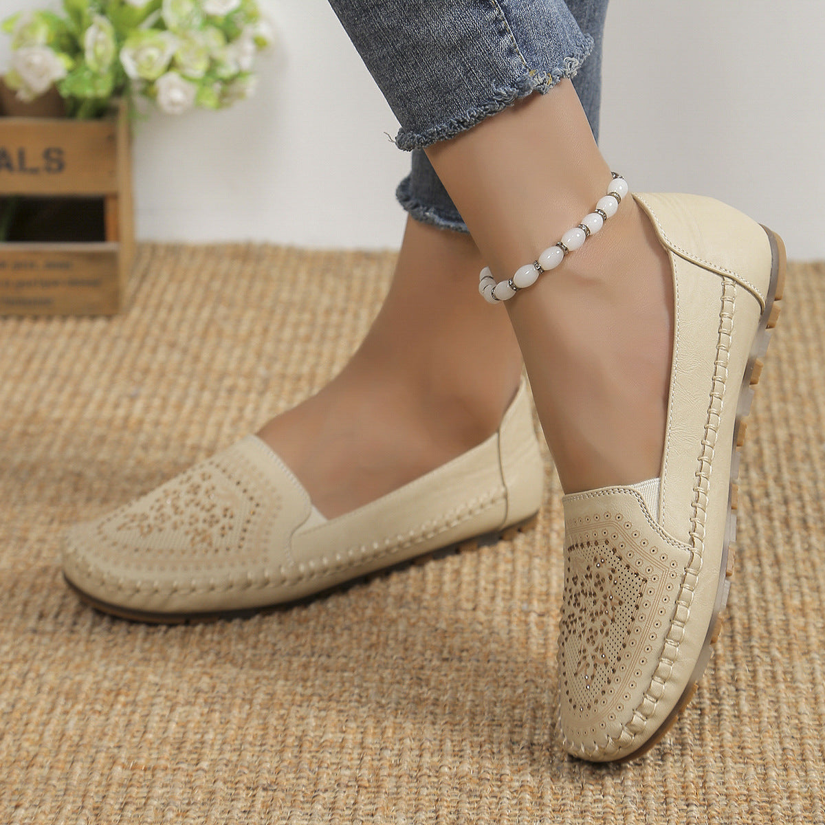 Beige Damen-Loafer aus Leder mit Lochmuster, getragen mit Jeans und Perlenfußkettchen, auf Juteteppich. Elegante, bequeme Freizeitschuhe.