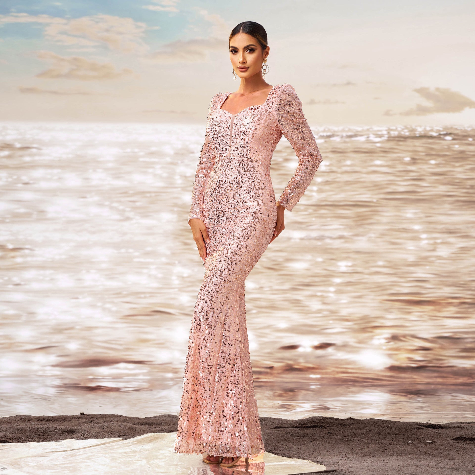 Elegantes Abendkleid in Rosa mit Pailletten, getragen von einer Frau am Strand bei Sonnenuntergang. Glamouröse Mode, Meereshintergrund, stilvolle Abendgarderobe.