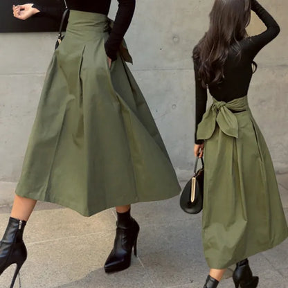 Grüner Maxirock mit hoher Taille und Schleife, kombiniert mit schwarzem Oberteil und Stiefeln. Modetrend Damenbekleidung Herbst/Winter.