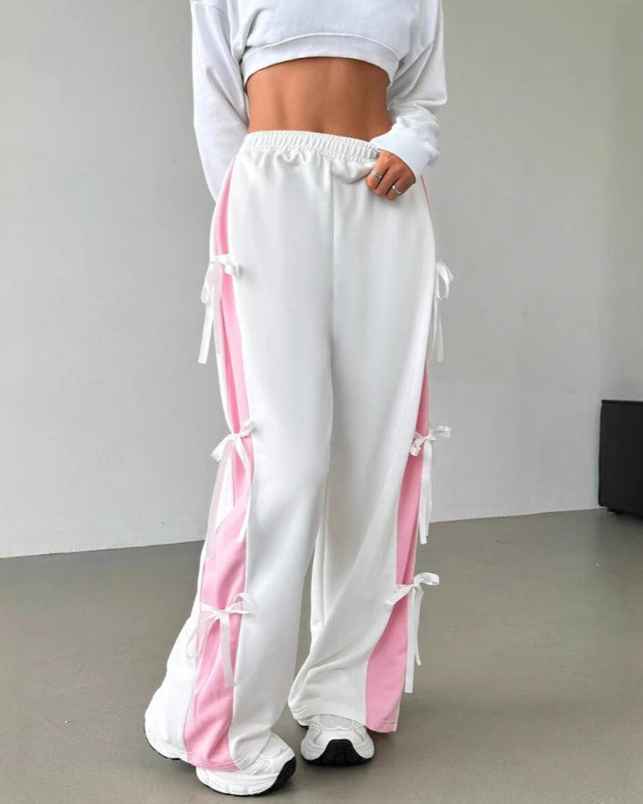 Weiße Jogginghose mit rosa Streifen und Schleifen, kombiniert mit weißem Crop-Top. Modetrend, sportlich, lässig, Damenbekleidung.