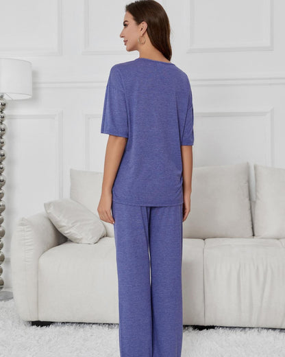 Frau in lila Pyjama-Set steht vor weißem Sofa in modernem Wohnzimmer. Bequeme Nachtwäsche, entspannte Atmosphäre, stilvolle Inneneinrichtung.