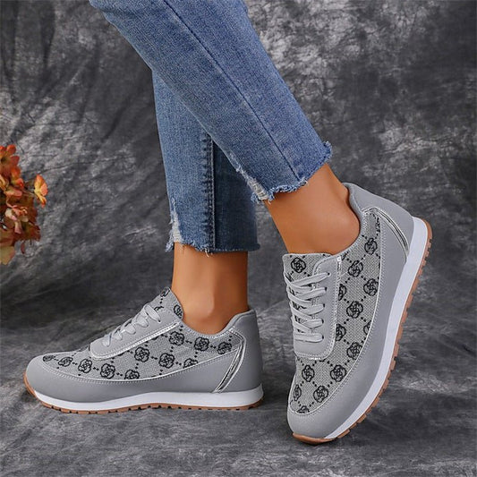 Graue Damen-Sneaker mit schwarzem Muster, kombiniert mit blauen Jeans. Modische Freizeitschuhe, ideal für Alltag und Sport.