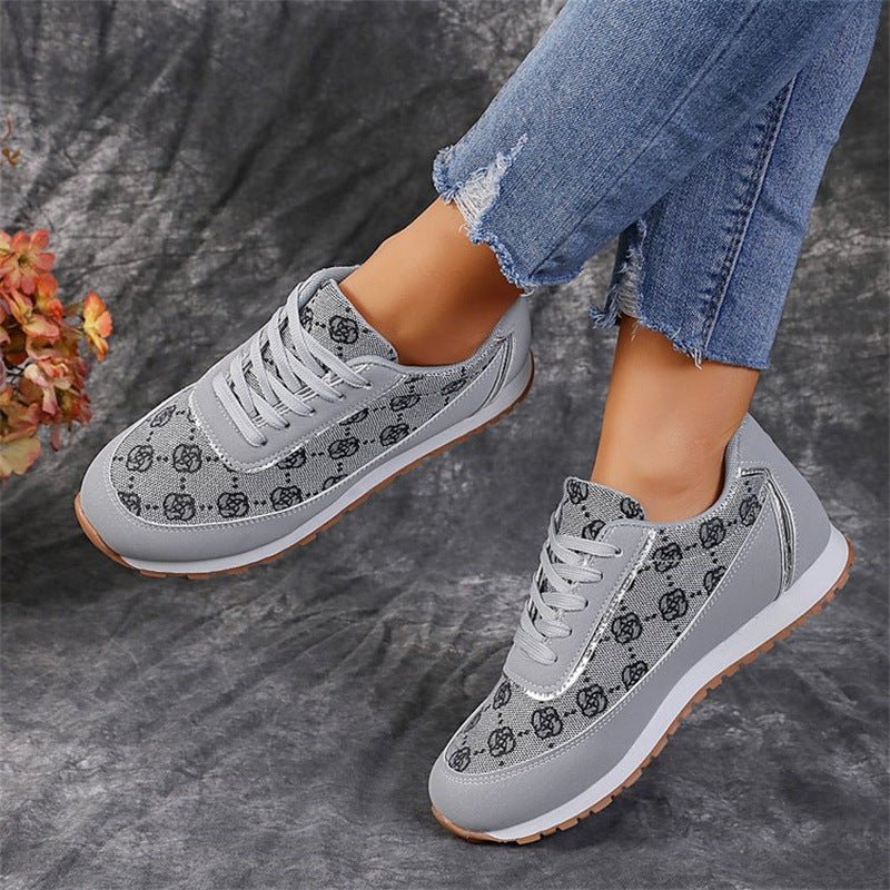 Graue Damen-Sneaker mit Blumenmuster, kombiniert mit zerrissenen Jeans. Modische Freizeitschuhe auf grauem Hintergrund.