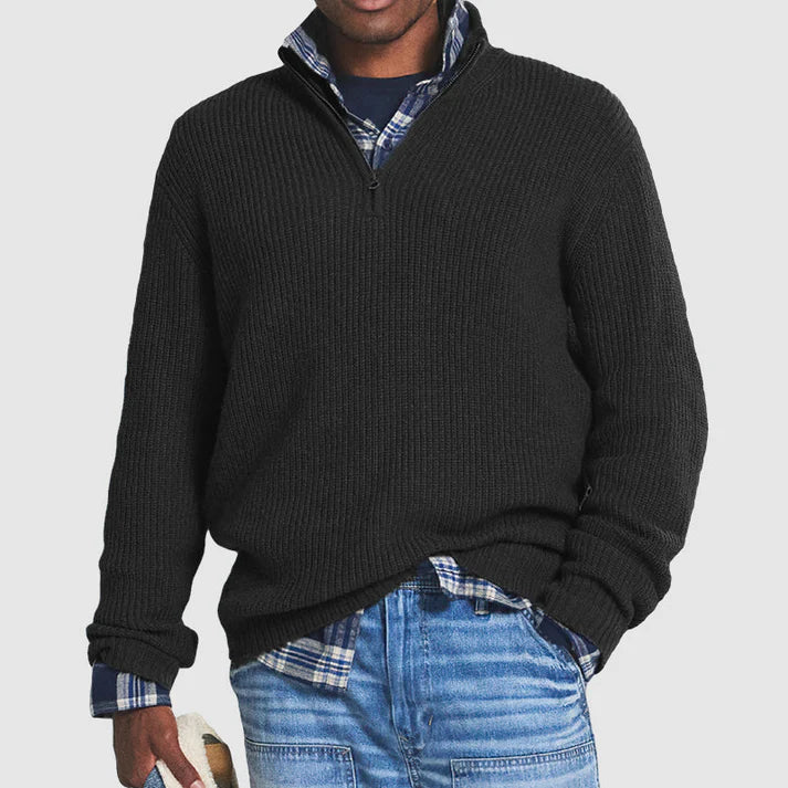 Mann in schwarzem Strickpullover mit Reißverschluss, kariertem Hemd und blauen Jeans. Modischer Freizeitlook für Herren.