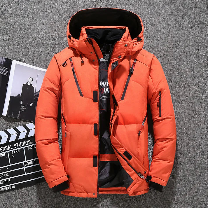 Orangefarbene Winterjacke mit Kapuze, Reißverschlüssen und Taschen, auf grauem Hintergrund. Perfekt für kaltes Wetter, modisch und funktional.