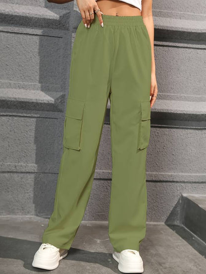 Grüne Cargo-Hose Damen, weites Bein, elastischer Bund, Seitentaschen, lässiger Stil, Streetwear, vor grauer Wand, modische Freizeitkleidung.