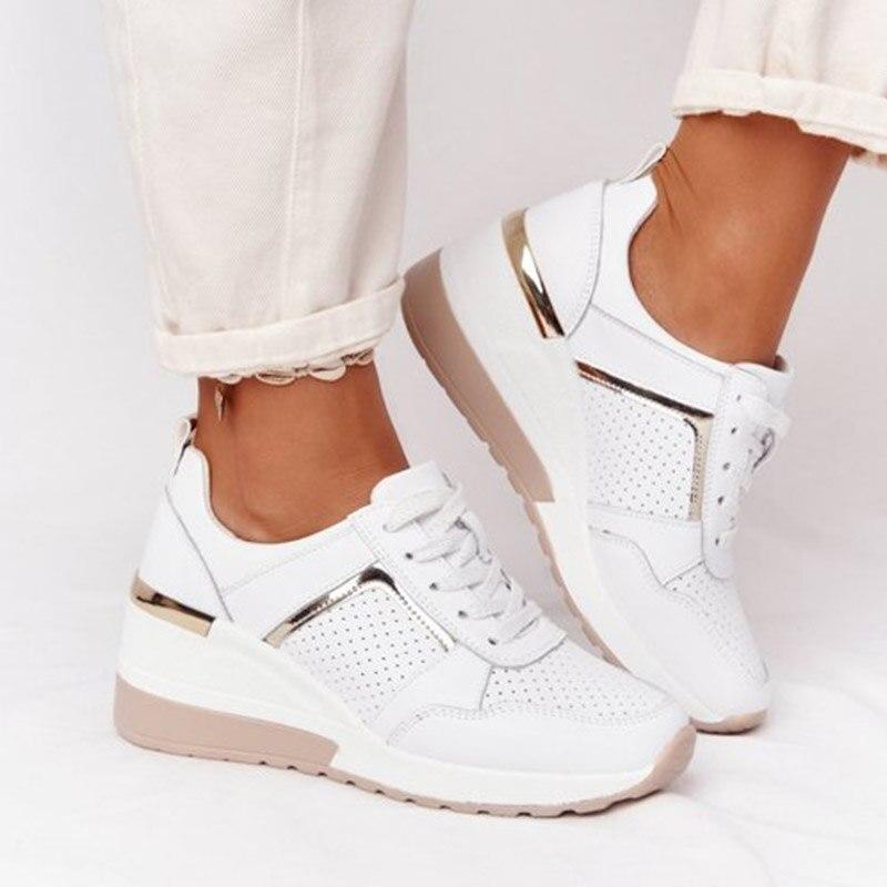 Weiße Damen-Sneaker mit Keilabsatz, perforiertem Design und goldenen Akzenten, getragen zu hellen Jeans. Modische Schuhe für Damen.