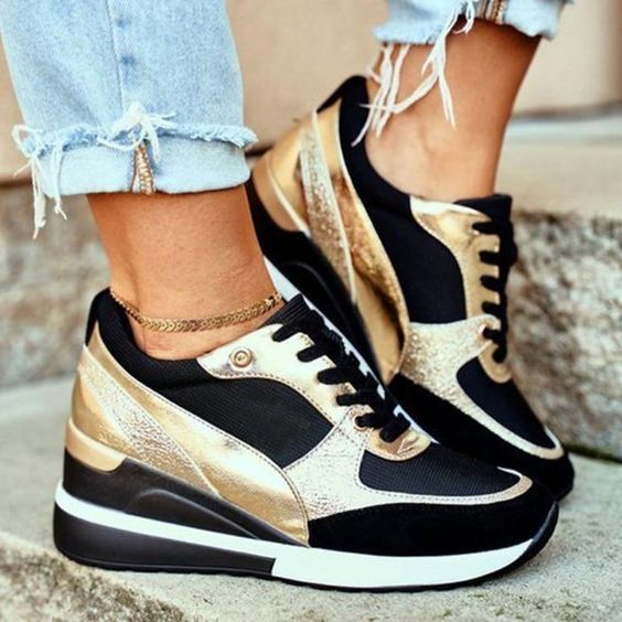 Schwarze und goldene Sneaker mit Keilabsatz, getragen mit zerrissenen Jeans. Modische Damen-Sportschuhe, trendiges Design, urbaner Stil.