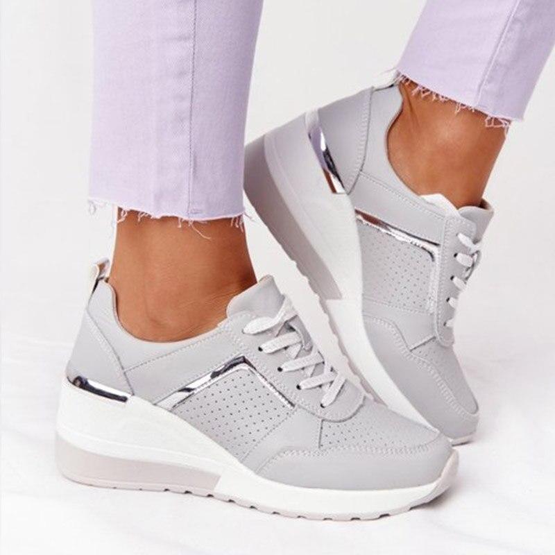 Graue Damen-Sneaker mit Keilabsatz, silbernen Details und perforiertem Design. Modische Freizeitschuhe, ideal für trendige Outfits.